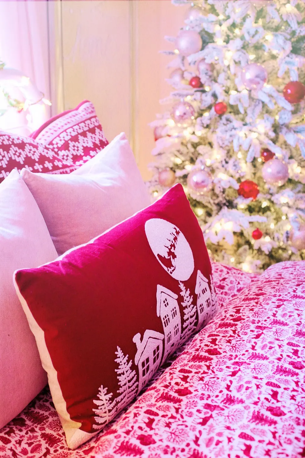Festive red and white pillows on a bed with a decorated Christmas tree in the background.