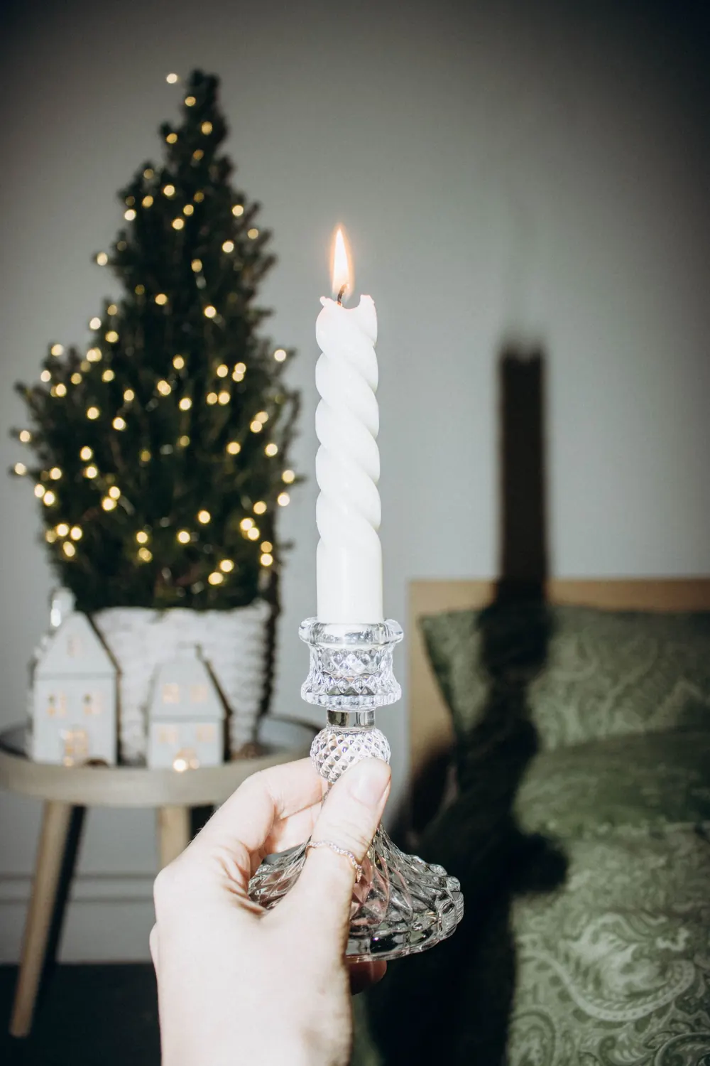 A hand holding a lit candle with a Christmas tree in the background, creating a festive ambiance.