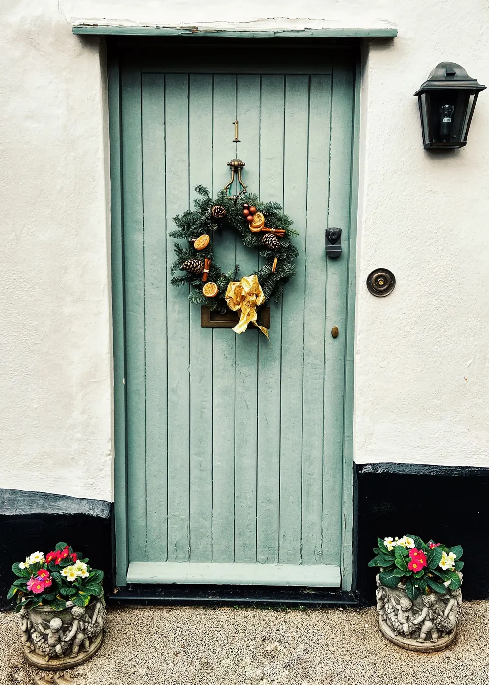 Charming green wooden door with a festive wreath, framed by colorful flower pots.