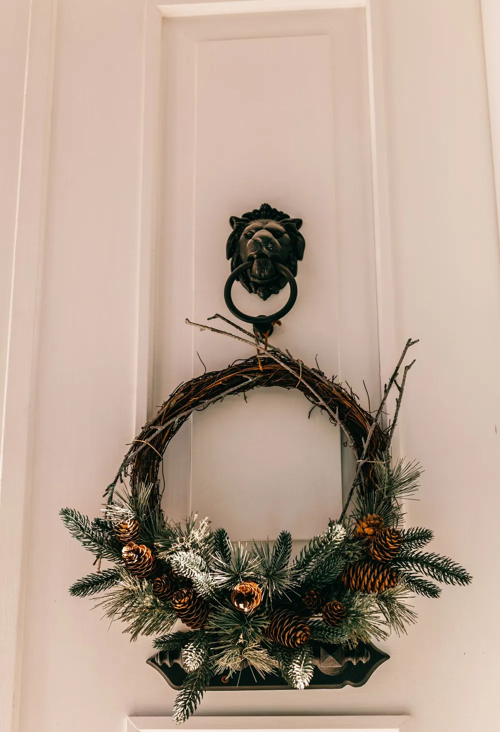Elegant Christmas wreath with pinecones and fir branches on a white door with a decorative knocker.