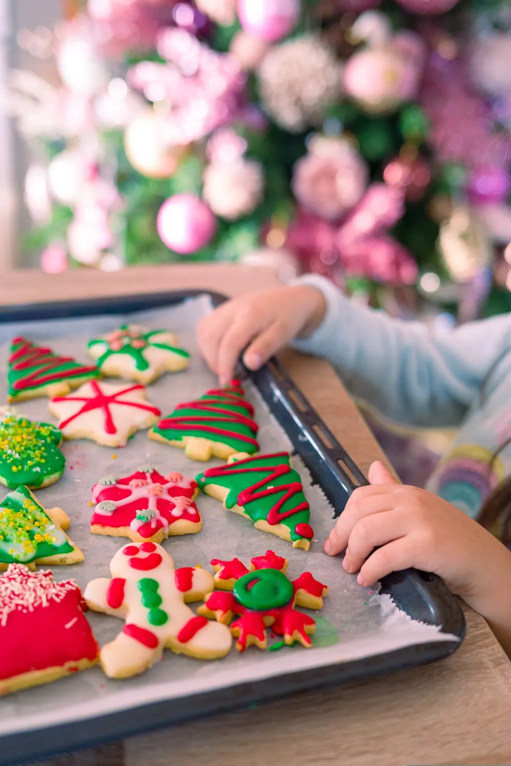 Child decorating Christmas cookies with festive holiday decorations in the background.