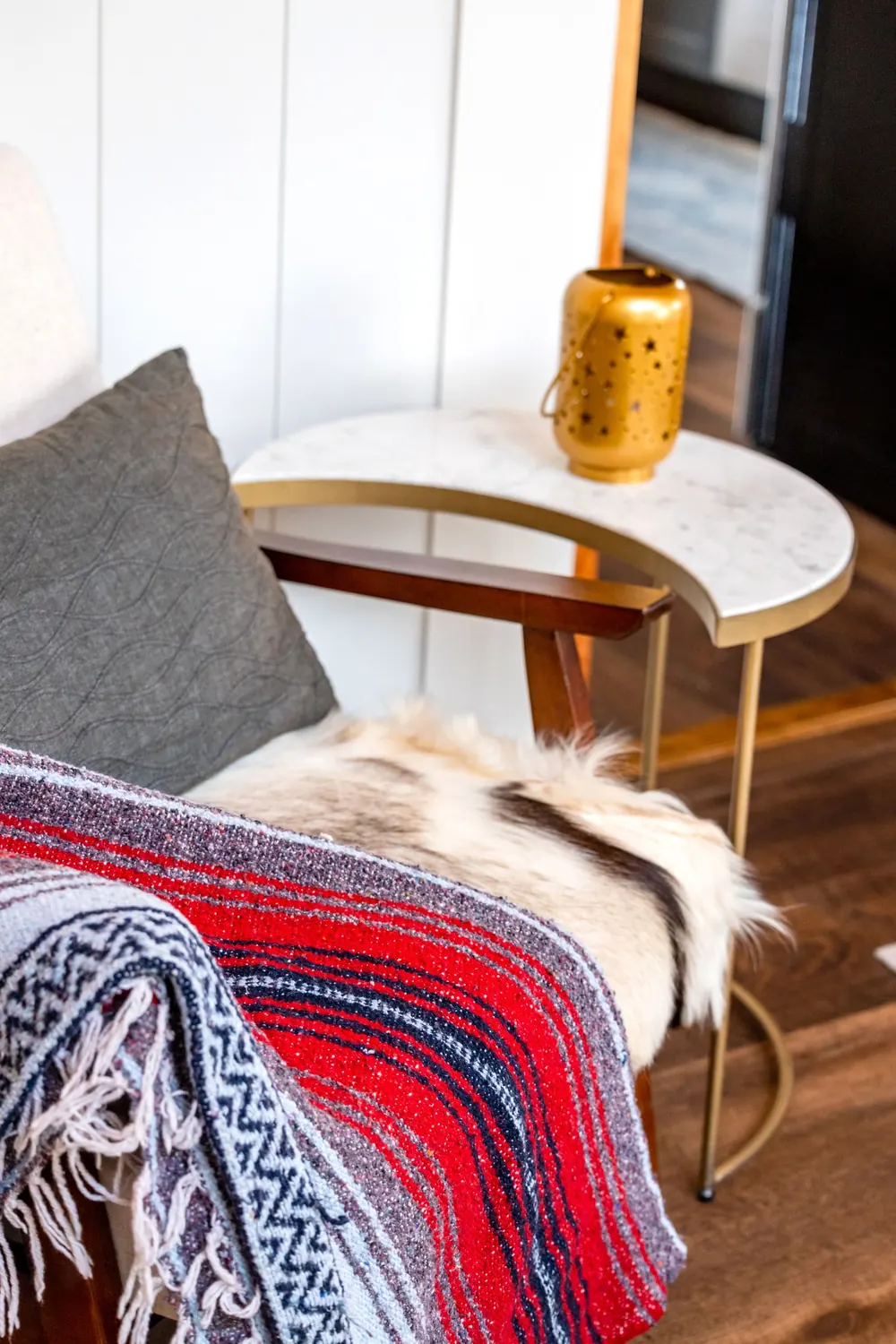 A cozy corner featuring a chair with a vibrant blanket and a stylish side table adorned with a decorative lamp.
