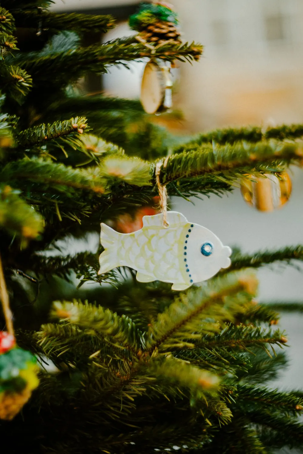 Decorative fish ornament hangs on a vibrant Christmas tree branch.