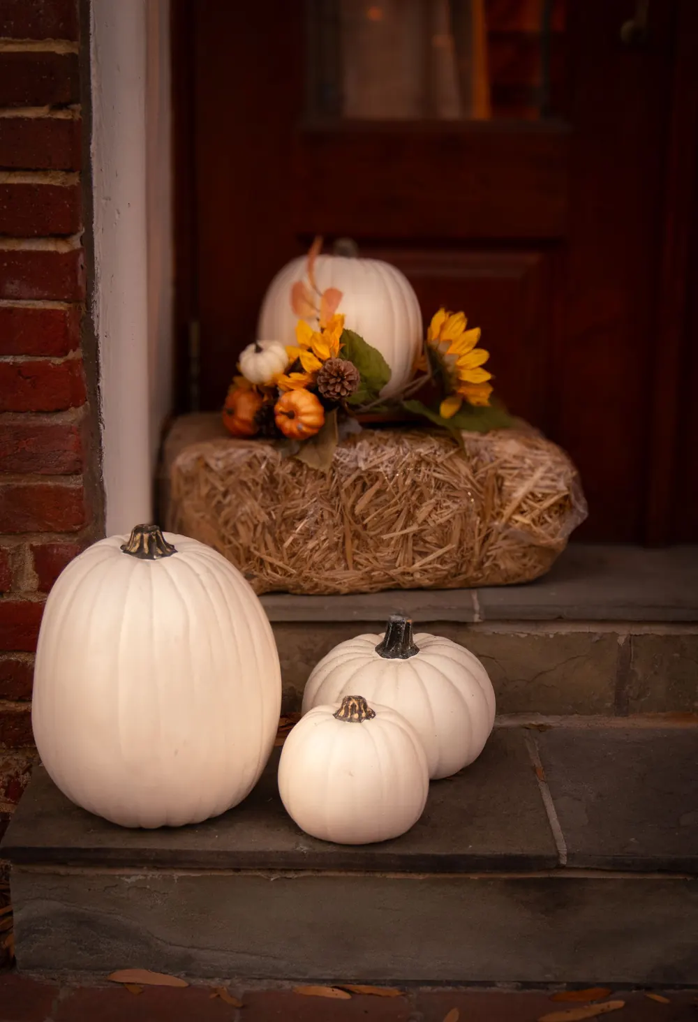 Charming fall porch setup featuring white pumpkins and autumn floral arrangement on hay bale.