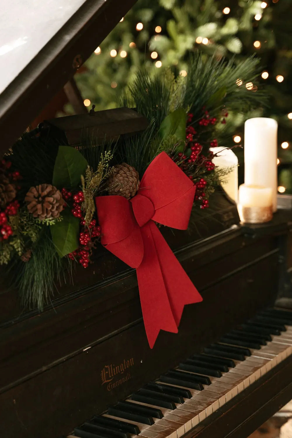 Elegant grand piano decorated with festive Christmas garland and red bow, indoors.