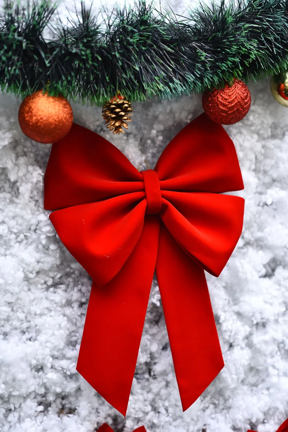 Vibrant red bow with ornaments and pine on snowy backdrop, ideal for holiday decoration themes.