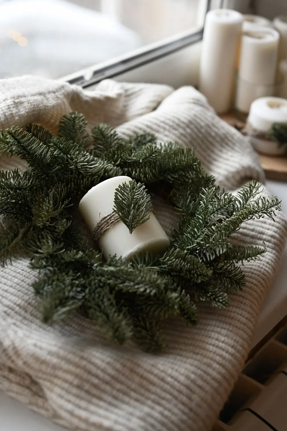 Rustic candle wrapped in a wreath by a window, evoking winter coziness.