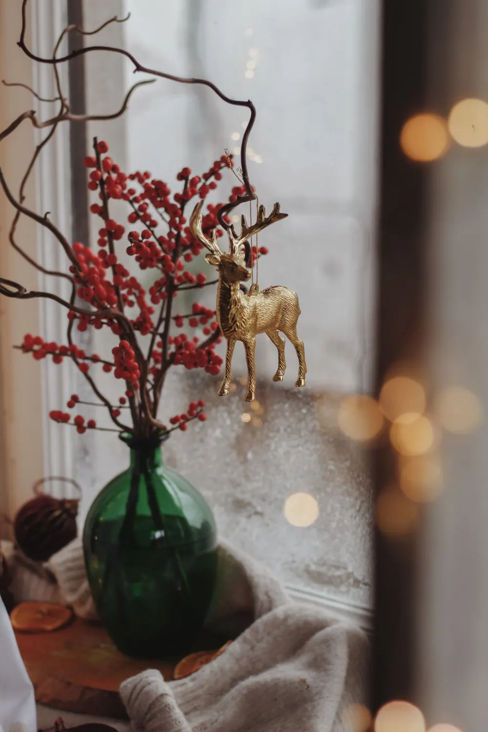 A warm festive scene with a golden deer ornament, red berries, and a vase on a windowsill.